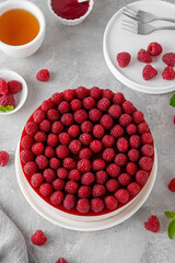 No baked raspberry cheesecake or raspberry cream mousse cake with jelly and fresh berries on top on a white plate on a gray concrete background. Summer cake.
