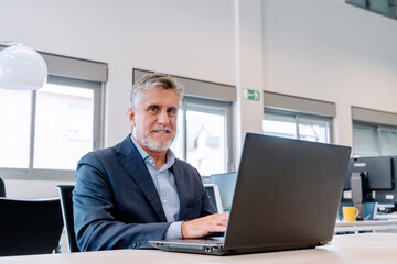 Mature businessman working with a laptop sitting on a desk in the office. Business concept.