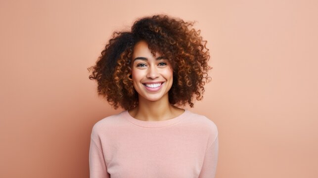 Portrait of young african woman standing with hands on waist and looking at camera. Confident stylish girl standing against peanch background. Happy young mixed race woman smiling i with copy space.