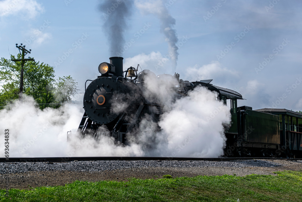 Wall mural A View of a Narrow Gauge Restored Steam Passenger Train Blowing Smoke and Lots of Steam, Starting To Pull Out of a Station on a Summer Day - Wall murals