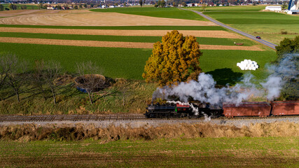 An Aerial Side View of a Steam Freight Train Traveling Thru Farmlands Blowing Smoke on a Sunny...