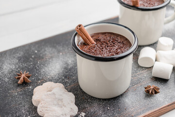 Homemade spicy hot chocolate drink with cinnamon stick, grated chocolate in enamel cup on wooden table with cookies, white marshmallows and star anise