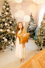 beautiful little girl laughs and stands near the Christmas trees with a star balloon. concept of happy childhood, making a wish for the new year and birthday.