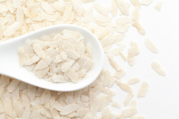 Macro close-up of Flattened rice (Oryza Sativa) or Poha on a white ceramic soup spoon. Top view, over a gradient background of itself.