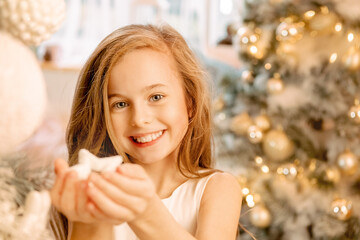 a cute little girl in a white dress holds a Christmas tree toy in her hand. child holding a star in his hands..