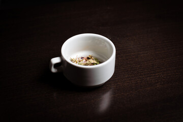 Herbal tea in a cup. Preparation of a drink from different herbs in a white cup on a dark background.