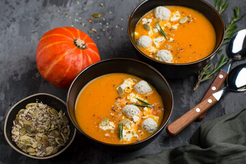 Two bowls of pumpkin puree soup with meatballs, pumpkin seeds, a sprig of rosemary, horizontal on a dark background. - obrazy, fototapety, plakaty