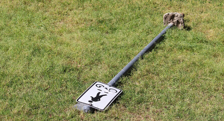 Sign post that has been pulled out of the ground and is now laying on the grass