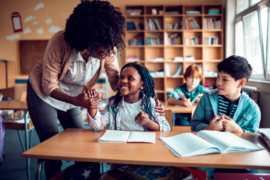 Teacher supporting little girl student at classroom