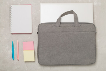 Grey stylish laptop bag with stationery on concrete background,top view