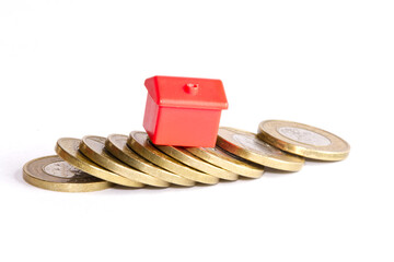 Single small red house standing on collapsed stack of coins on white background. 