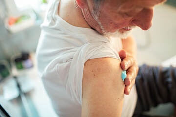 Close up senior man putting ointment on shoulder in bathroom - obrazy, fototapety, plakaty