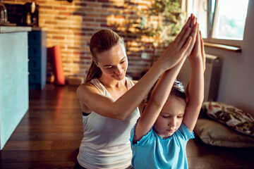 Beautiful young woman and her little daughter doing yoga together at home