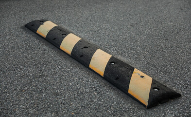 High-angle view of yellow speed bump on asphalt road, cautionary traffic sign nearby