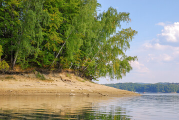 View of the water and the sandy shore of Lake Solina in summer. There is a forest around. Panorama of the Bieszczady Mountains, Poland.