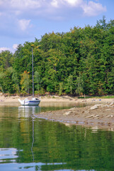 A white sailboat moored at the shore. Sailing a yacht on Lake Solina in summer. Panorama of the Bieszczady Mountains, Poland.