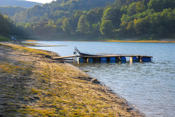 View of the wooden bridge on barrels on Lake Solina. There's a forest all around. People on the shore. Summer in the Bieszczady Mountains, Poland.