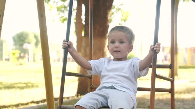 little boy swings on a swing. concept of a happy childhood and loving family. a child in white clothes swings on a swing on lifestyle the playground, the boy is being filmed by his parents