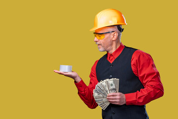 A Construction Worker Enjoying His Break with a Cup of Coffee and Extra Cash. A man in a hard hat holding a cup and money