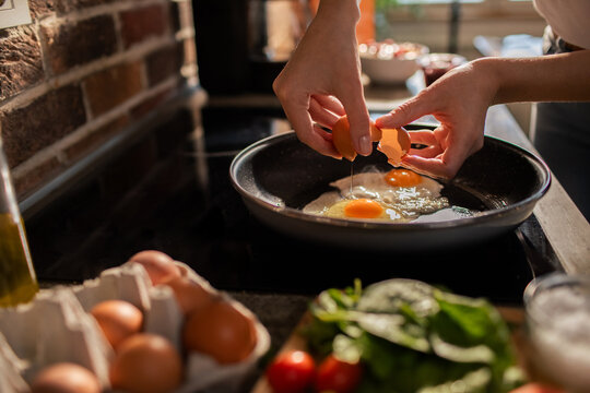 Hands cracking shell in pan making fried eggs in kitchen