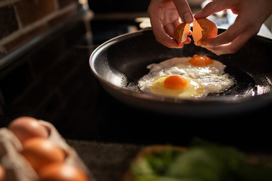 Hands cracking shell in pan making fried eggs in kitchen