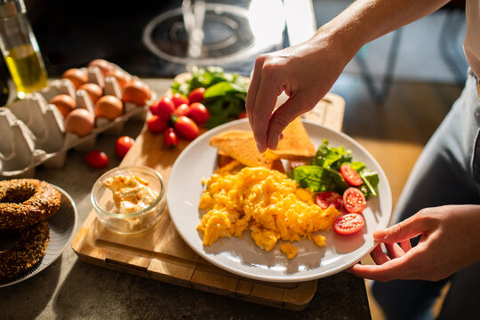 Woman hand adding salt to plate of scrambled eggs with salad