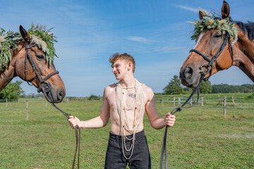 Portrait d'un jeune homme tenant des chevaux avec des colliers de fleurs et de feuilles - obrazy, fototapety, plakaty