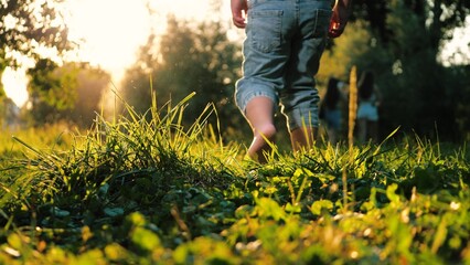 Little contented child joyfully dashes barefoot on grass in park during warm weather. In meadow...