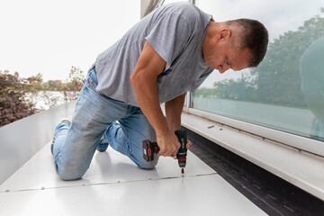 Construction worker installing new metal sheet roof. Man with cordless drill screws the roofing...