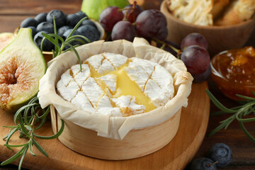 Tasty baked brie cheese and products on wooden table, closeup