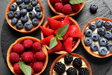 Tartlets with different fresh berries on slate plate, flat lay. Delicious dessert