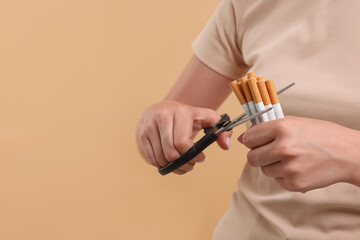 Stop smoking concept. Woman cutting cigarettes on light brown background, closeup. Space for text