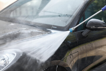 Washing auto with high pressure water jet at outdoor car wash, closeup