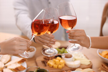 People clinking glasses with rose wine above wooden table indoors, closeup