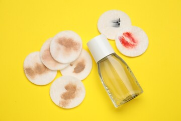 Bottle of makeup remover and dirty cotton pads on yellow background, flat lay