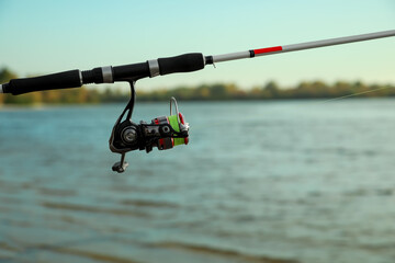 Fishing rod with reel near river, space for text