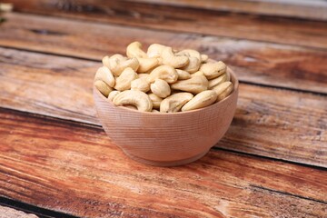 Tasty cashew nuts in bowl on wooden table