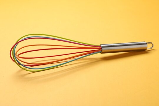 Bright whisk on yellow background. Kitchen tool