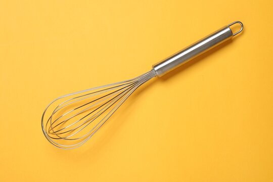 Metal whisk on yellow background, top view. Kitchen tool