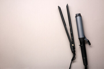 Curling iron and hair straightener on grey background, flat lay. Space for text