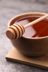 Delicious honey in bowl and dipper on grey textured table, closeup