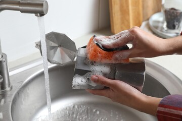 Woman washing moka pot (coffee maker) above sink in kitchen, closeup