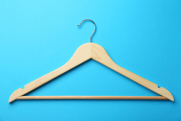 Wooden hanger on light blue background, top view