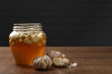 Honey with garlic in glass jar on wooden table. Space for text