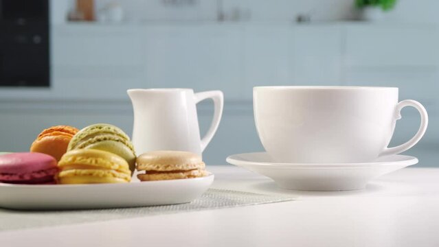 bright kitchen, on the table there is coffee with a milk jug and a plate with macarons. Breakfast, sugar consumption and coffee consumption or coffee enjoyment