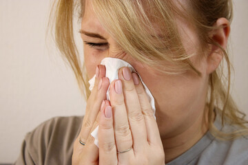 Close up of sick woman sneezing in a tissue at home