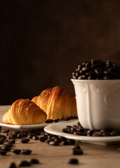 Fotografia conceptual de  tasa de porcelana  llenas de granos de cafe con dos croasaints sobre mesa de madera y fondo marron