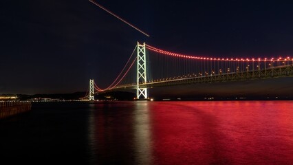 ライトアップされた明石海峡大橋と赤く染まる水面のコラボ情景 - obrazy, fototapety, plakaty