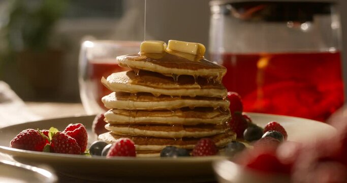 Maple syrup syrup or honey pours in a thin stream onto the perfect tasty stack of pancakes. No people, advertising cinematic. Healthy lifestyle with individual approach to cooking and domestic life