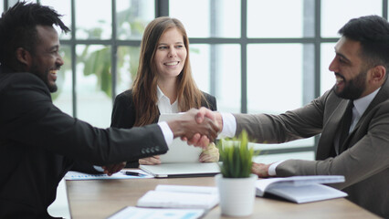 Business people shaking hands while sitting at the desk in office